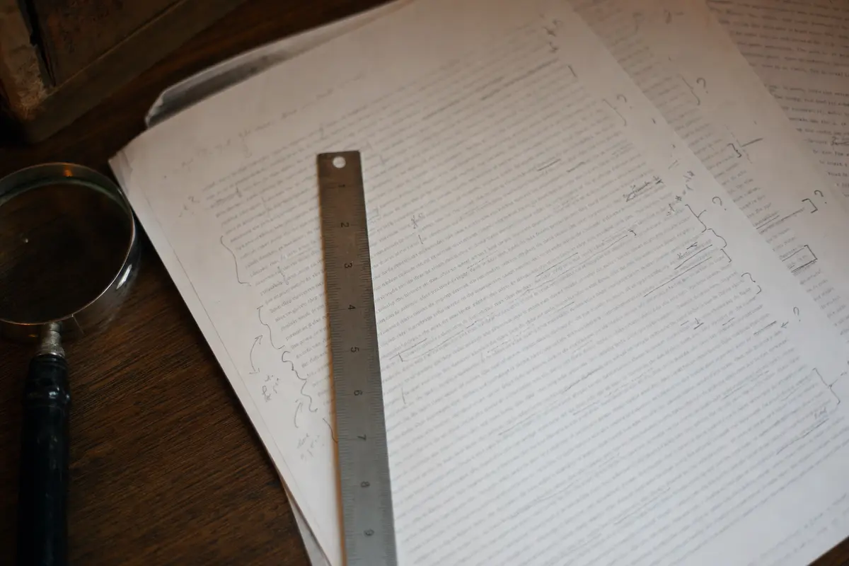 Annotated research pages spread across a wooden table under a lamp