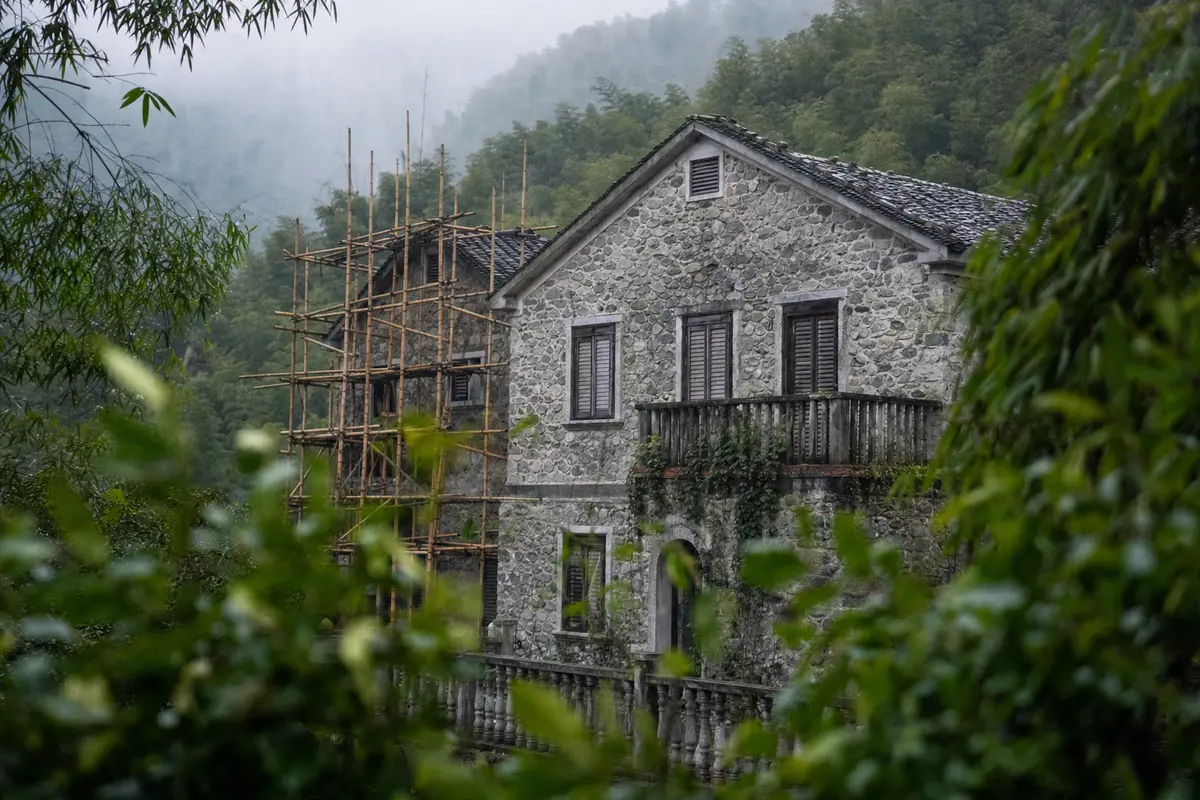 A stone villa under scaffolding on a misty bamboo hillside