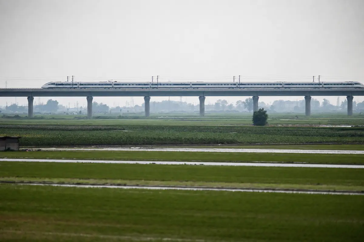 A high-speed train crossing a viaduct over flat green farmland