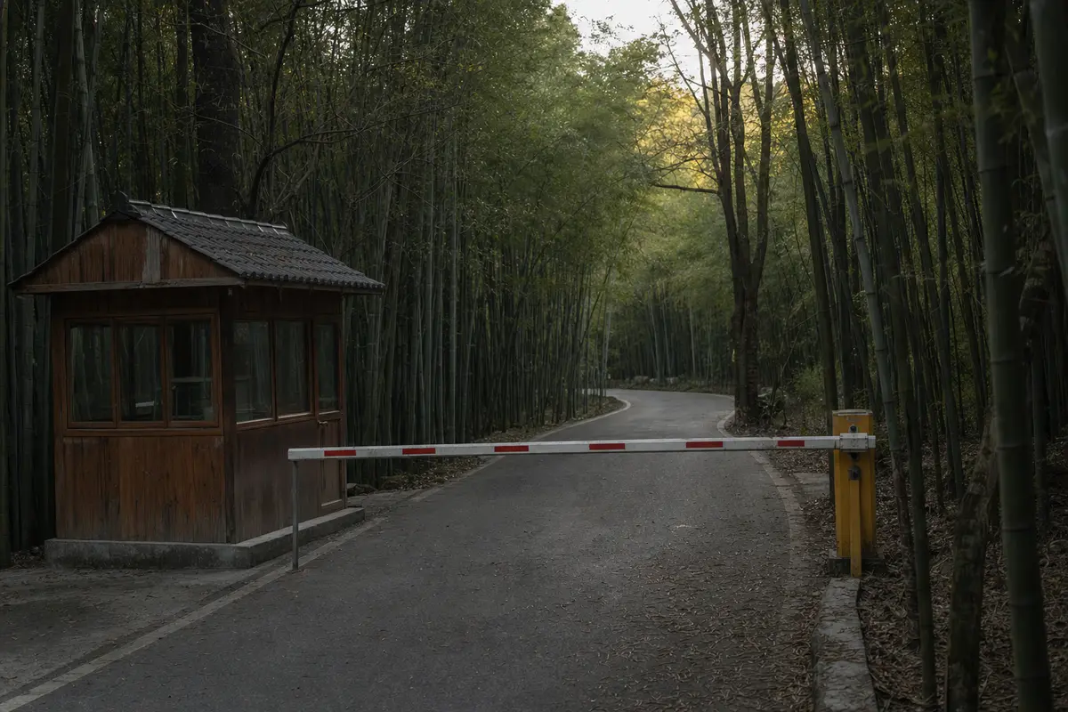 A barrier gate closed across a mountain road with bamboo forest on both sides