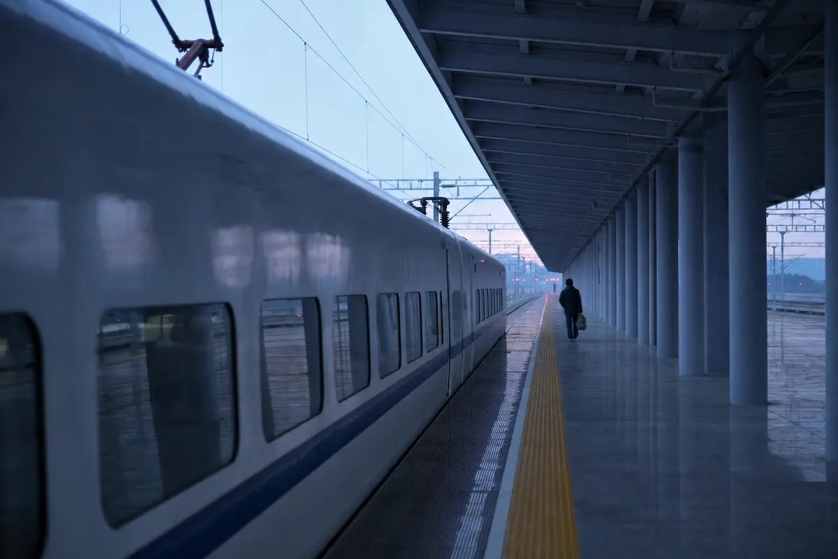 An almost empty high-speed rail platform before sunrise with a white train waiting