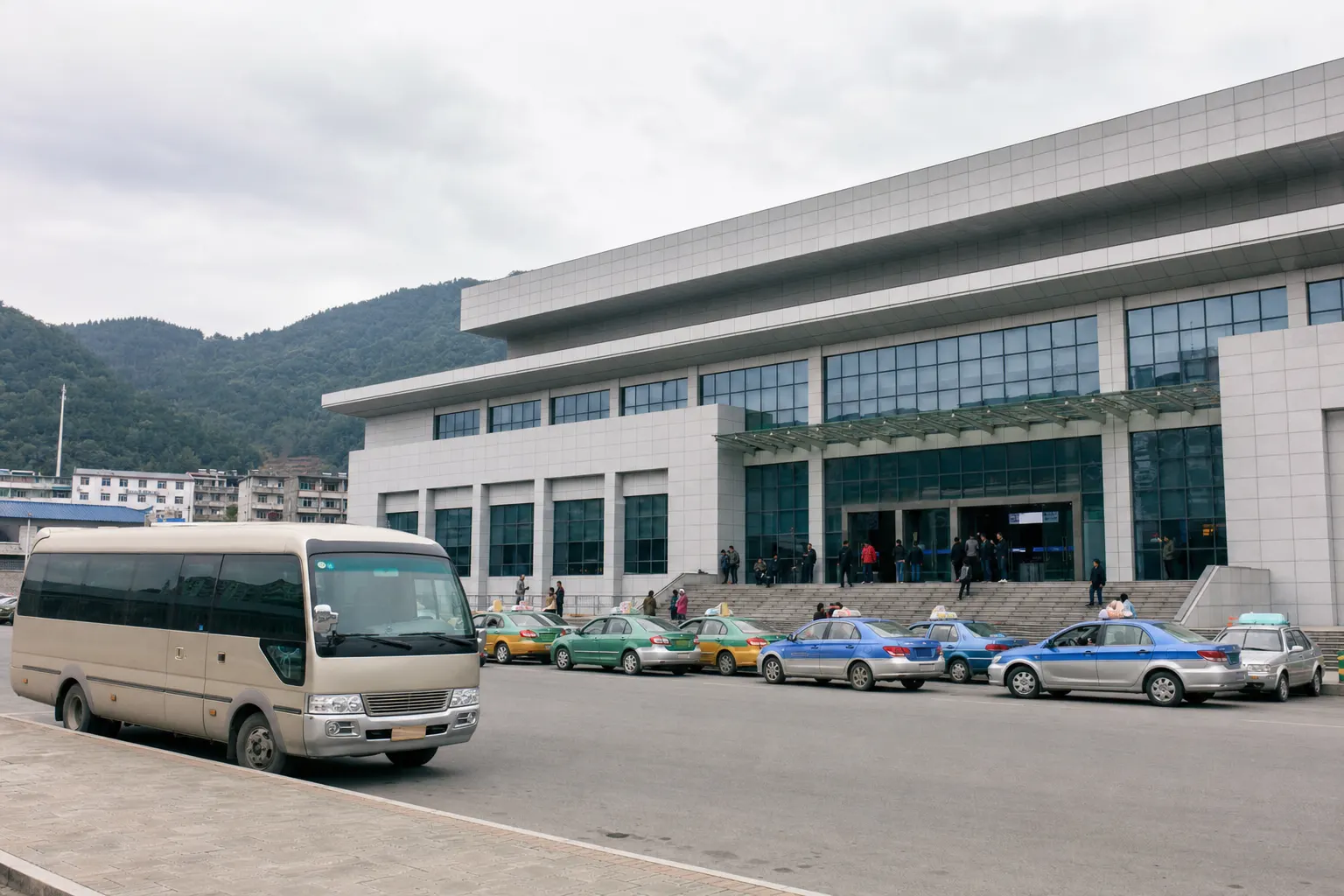 A minibus and a line of taxis waiting outside a small modern Chinese railway station
