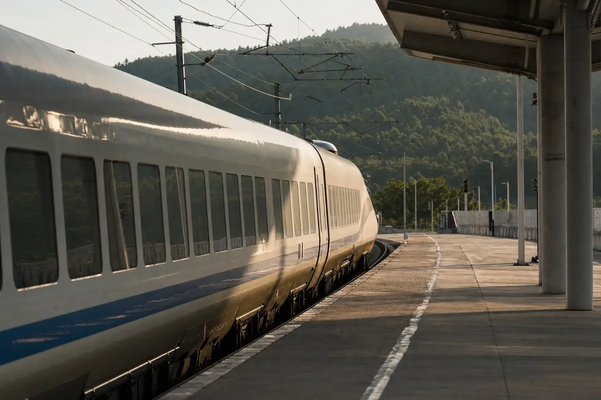 A white high-speed train pulling into a small provincial platform in afternoon sun