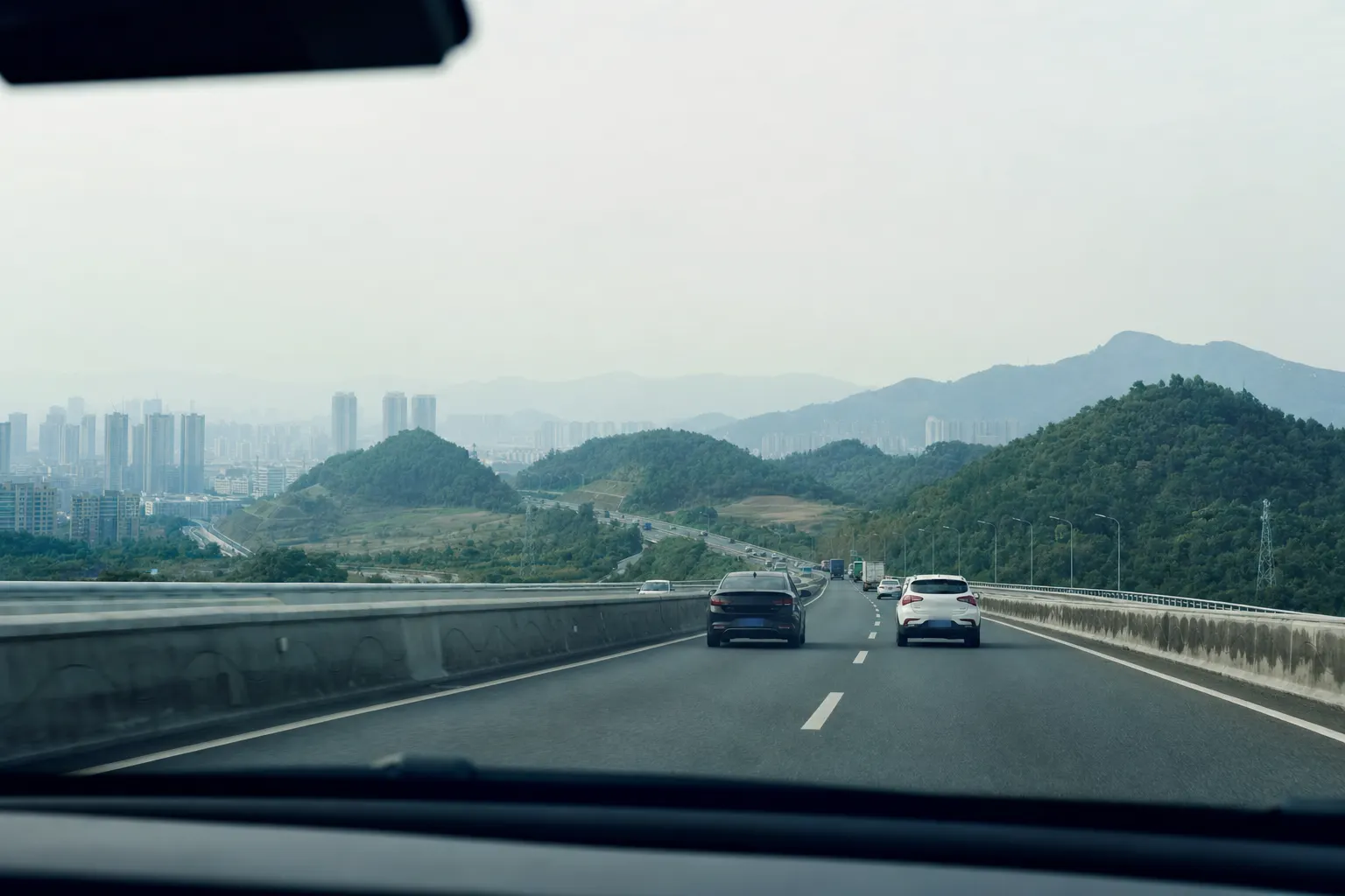 The view from a car on an elevated expressway leaving a hazy Chinese city for green hills