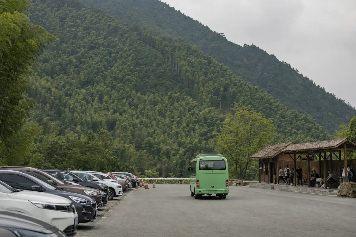 A car park and waiting shelter at the foot of a bamboo mountain with a shuttle bus leaving