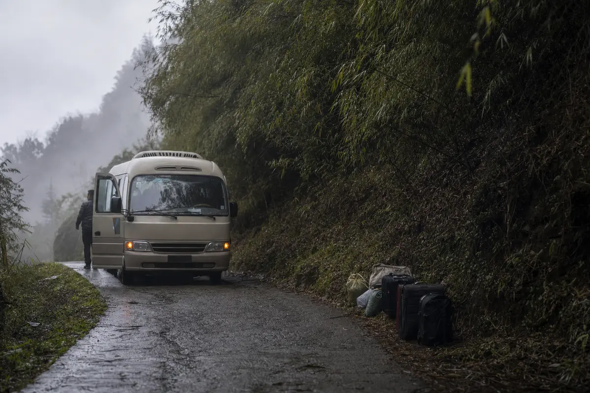 A minibus on a narrow mountain lane with luggage stacked on the verge