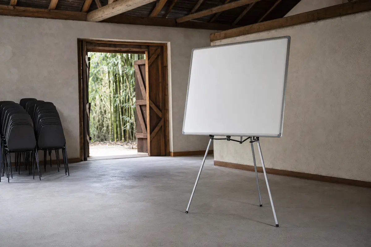 A whiteboard and stacked chairs in a plain converted barn meeting space