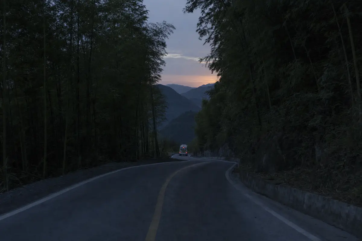 A shuttle bus heading downhill on an empty mountain road at dusk