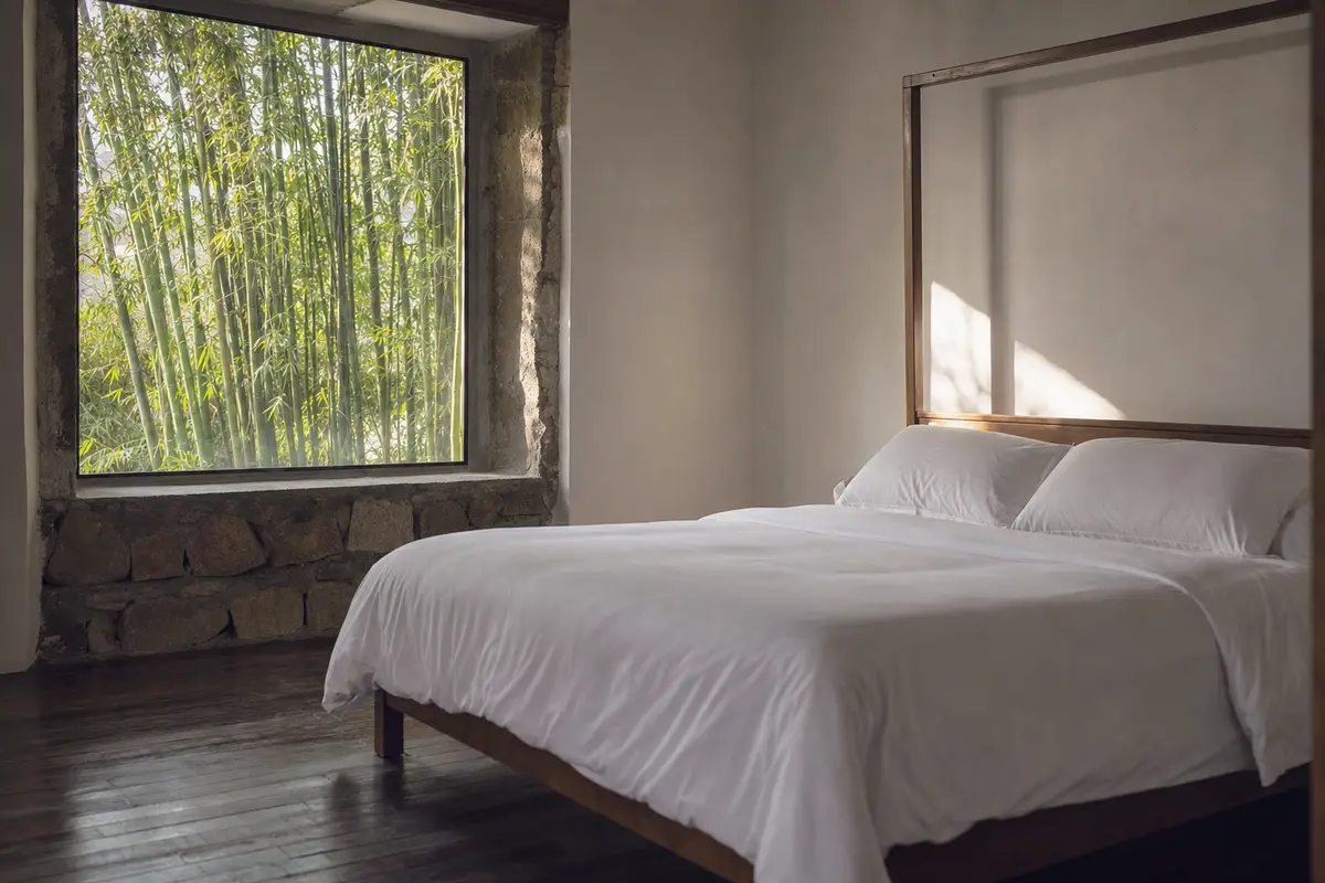 A plain guest bedroom in a converted stone villa with bamboo filling the window