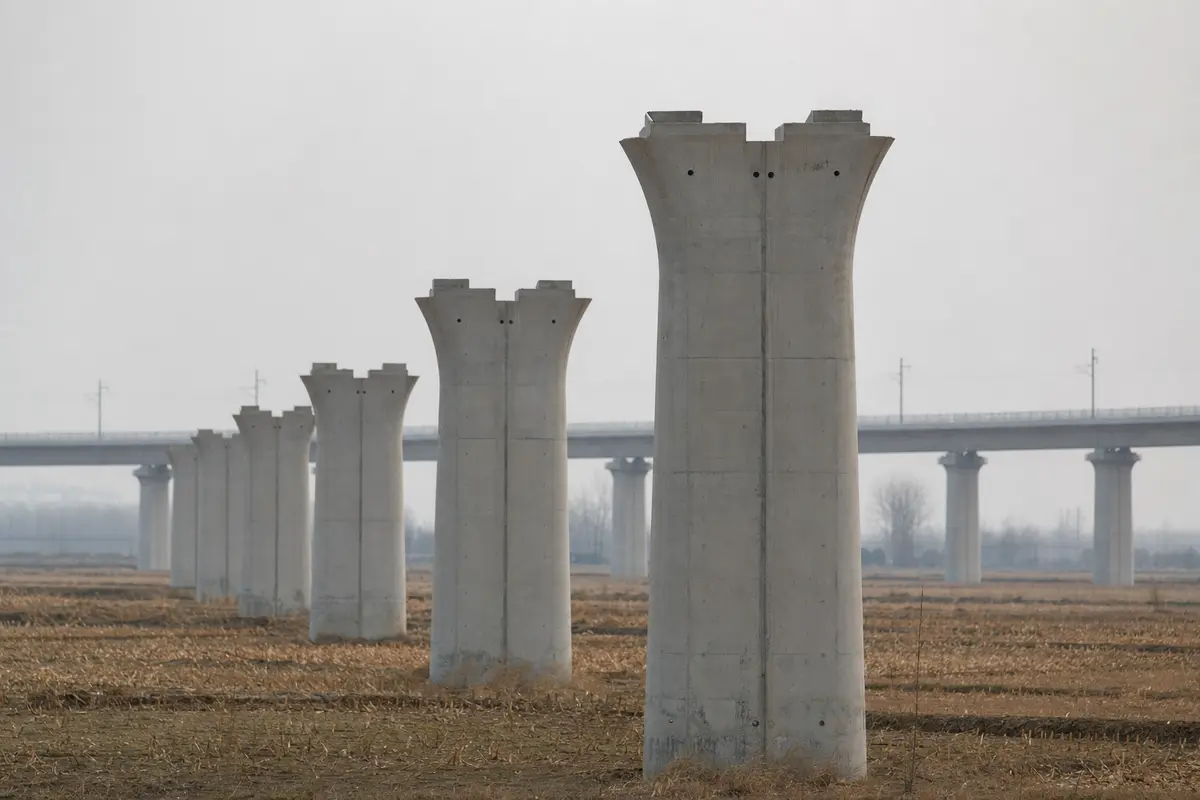 New railway viaduct piers crossing flat farmland towards a completed elevated track