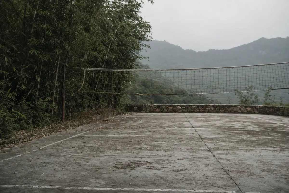 A cracked concrete sports court with a sagging net on a mountain terrace