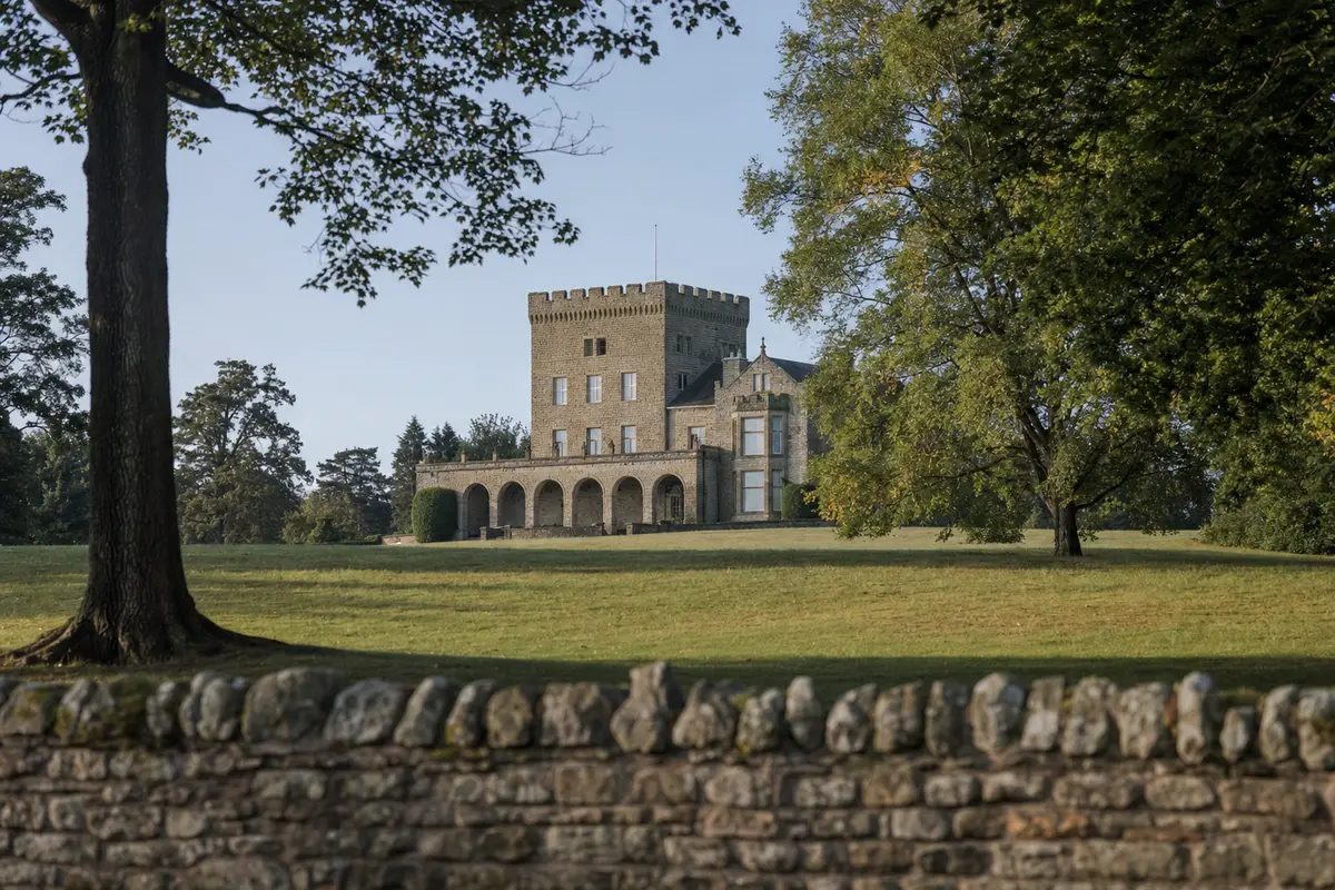A stone villa with a castellated tower and arched openings seen across a lawn
