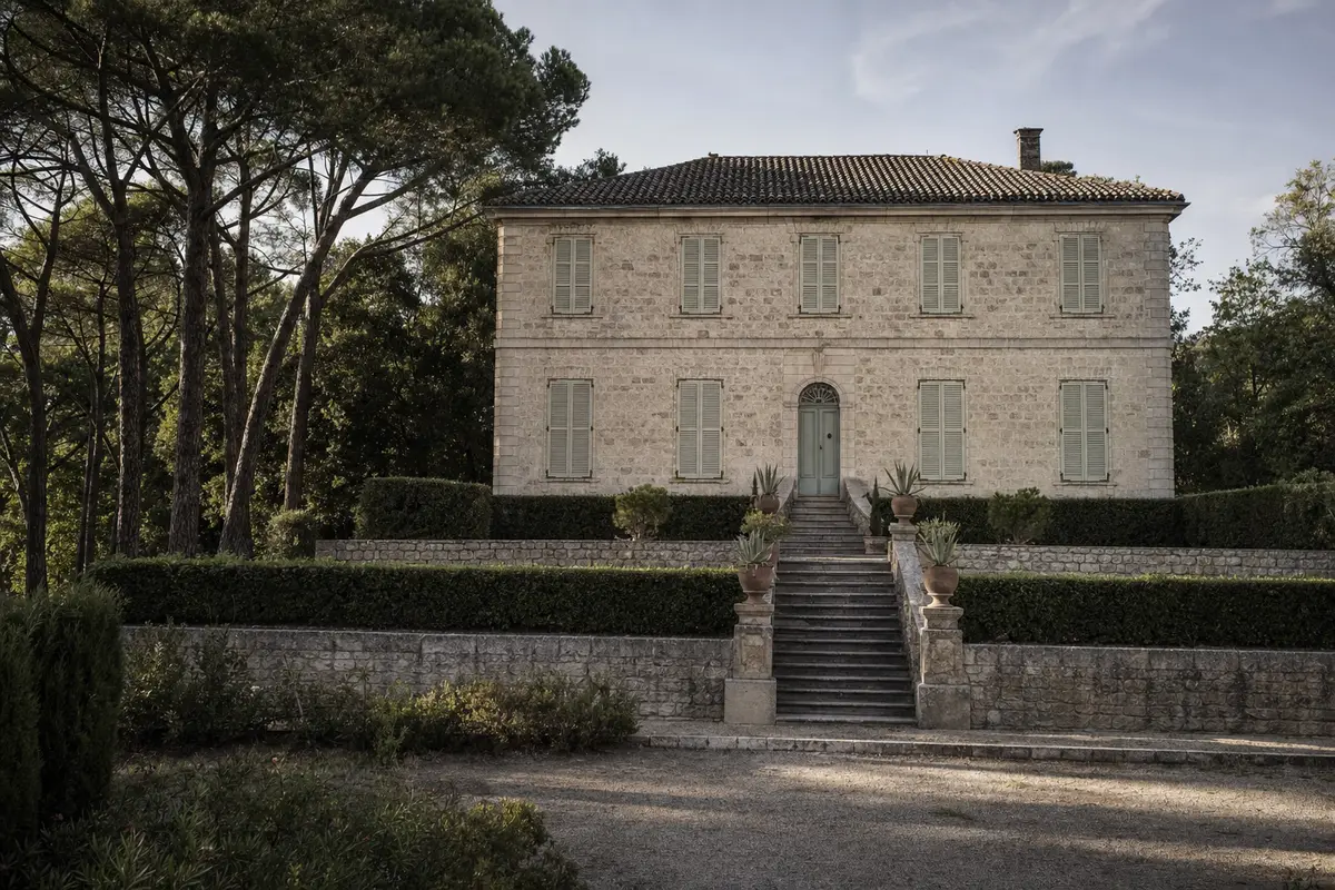 A symmetrical two storey stone house on a terrace with steps rising to the entrance