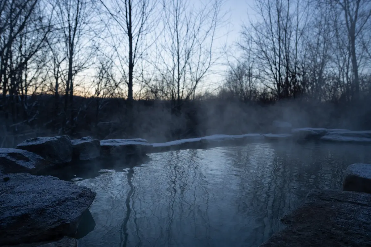 Steam rising from a still dark outdoor pool at dawn