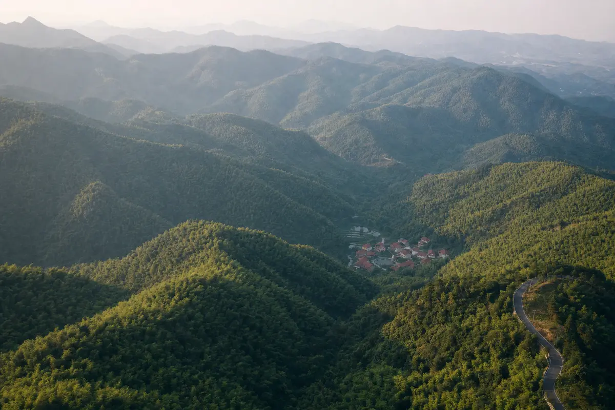 An aerial view over a forested mountain massif with roofs scattered in one valley