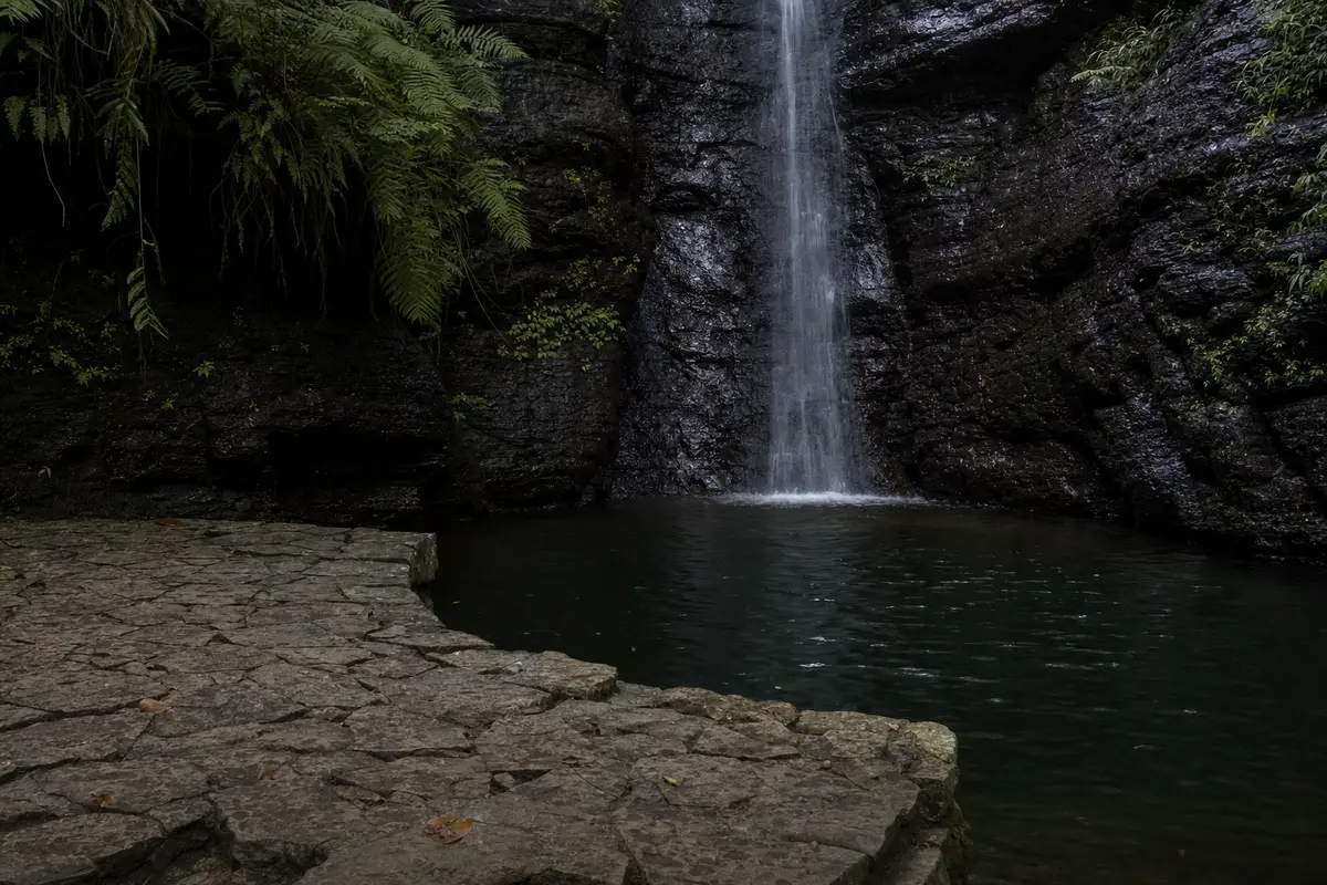 A dark still pool below a small waterfall in a rock cleft with a stone viewing platform