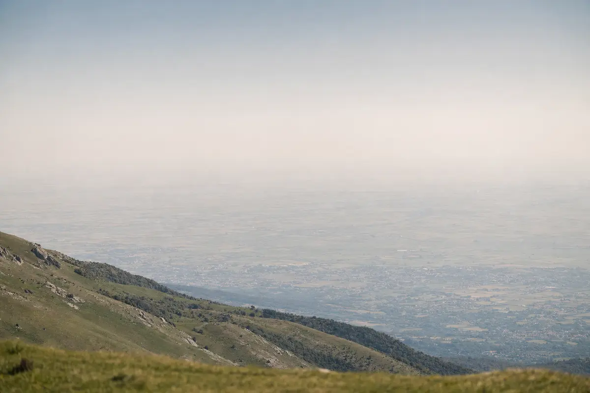 The view from a mountain shoulder down onto a hazy plain far below