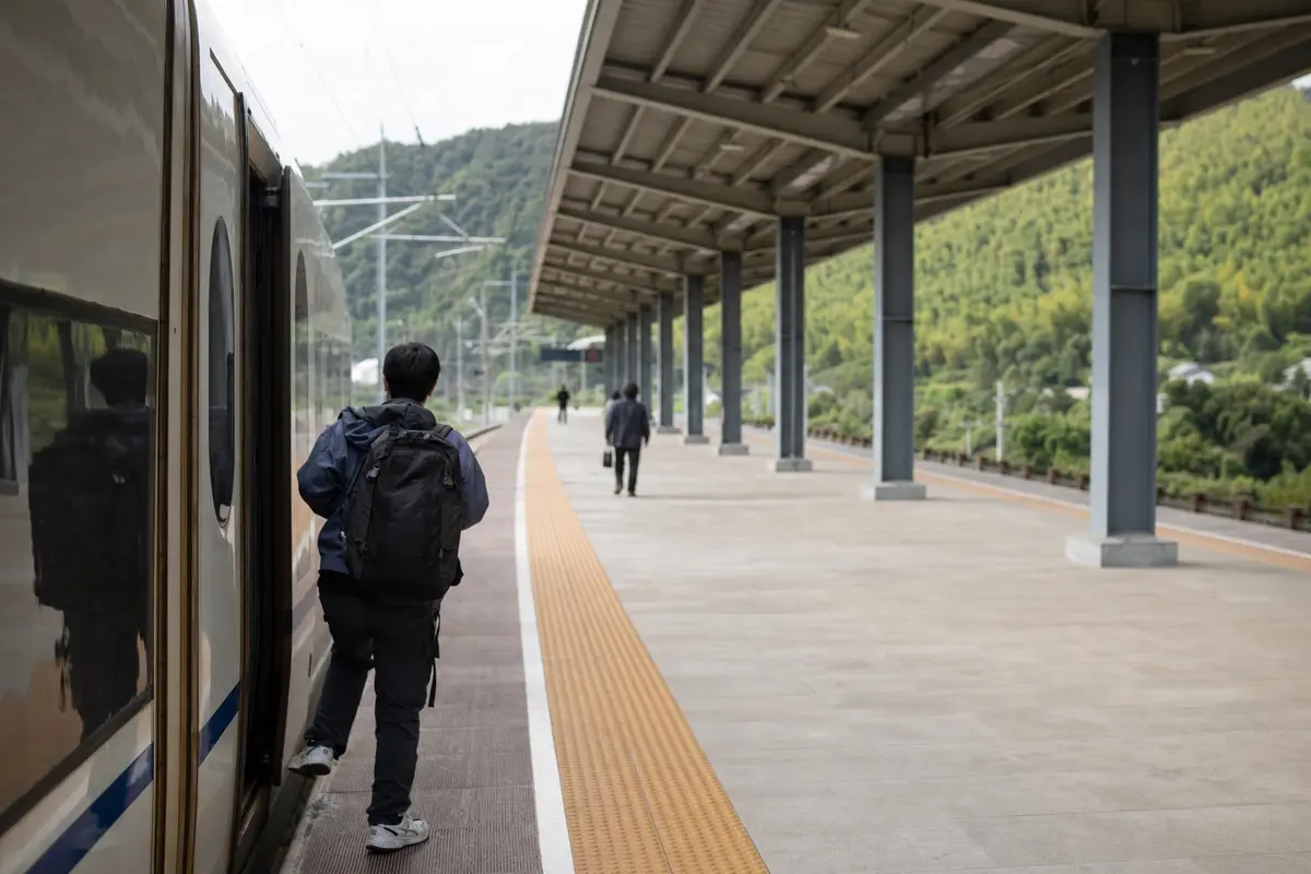 A traveller with a rucksack stepping down from a train onto a small platform