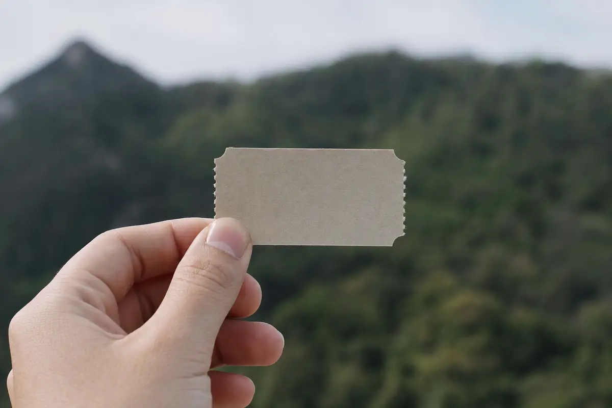 A hand holding a plain paper ticket stub against a blurred green background