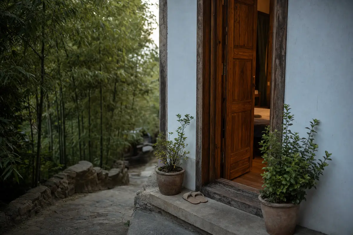 An open guesthouse doorway with slippers on the step and potted plants either side