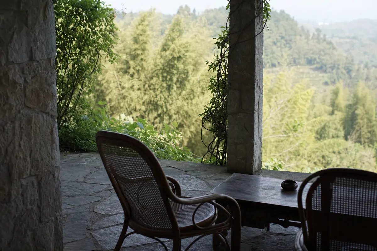 A shaded stone villa veranda with cane chairs looking over a bamboo valley in summer