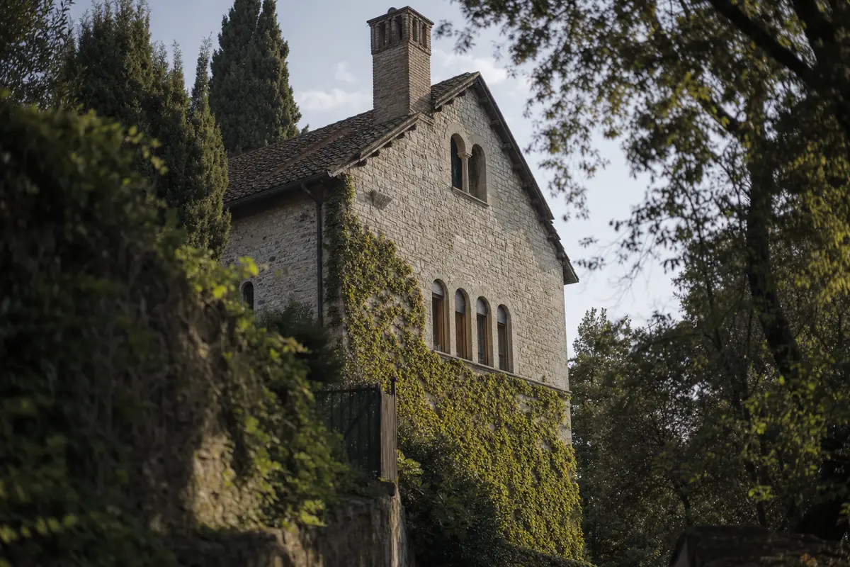 A stone villa gable with a tall chimney and arched windows seen from a lane below