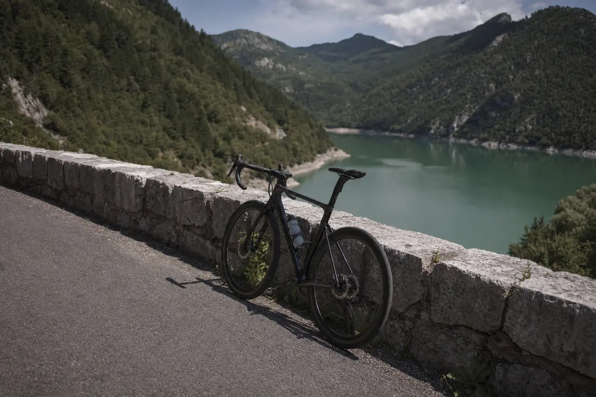 A bicycle leaning on a stone parapet above a still green reservoir among forested slopes
