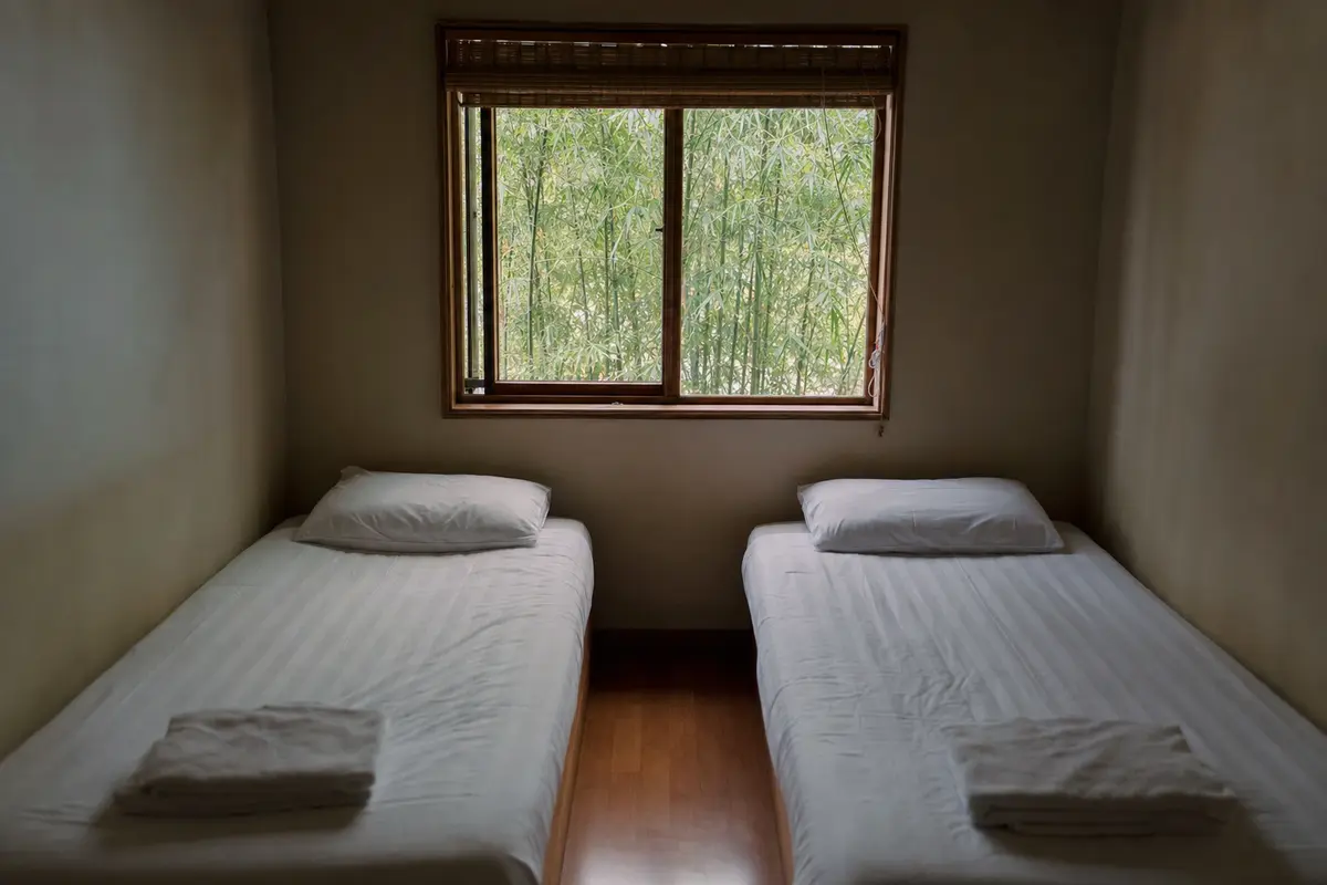 A simple twin room in a mountain guesthouse with plain bedding and a small window