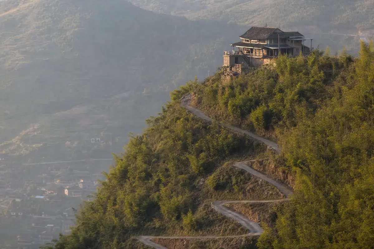 A guesthouse standing alone above a village with a lane switchbacking up to it
