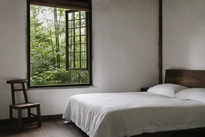 A plain guest room with white walls, a linen-covered bed and a window open onto bamboo