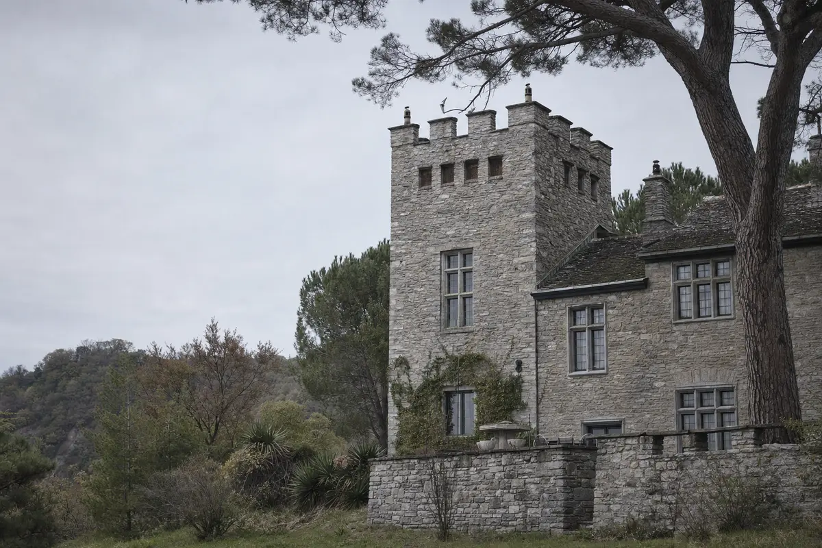 A stone villa with a square castellated tower and heavy mullioned windows on a wooded hillside