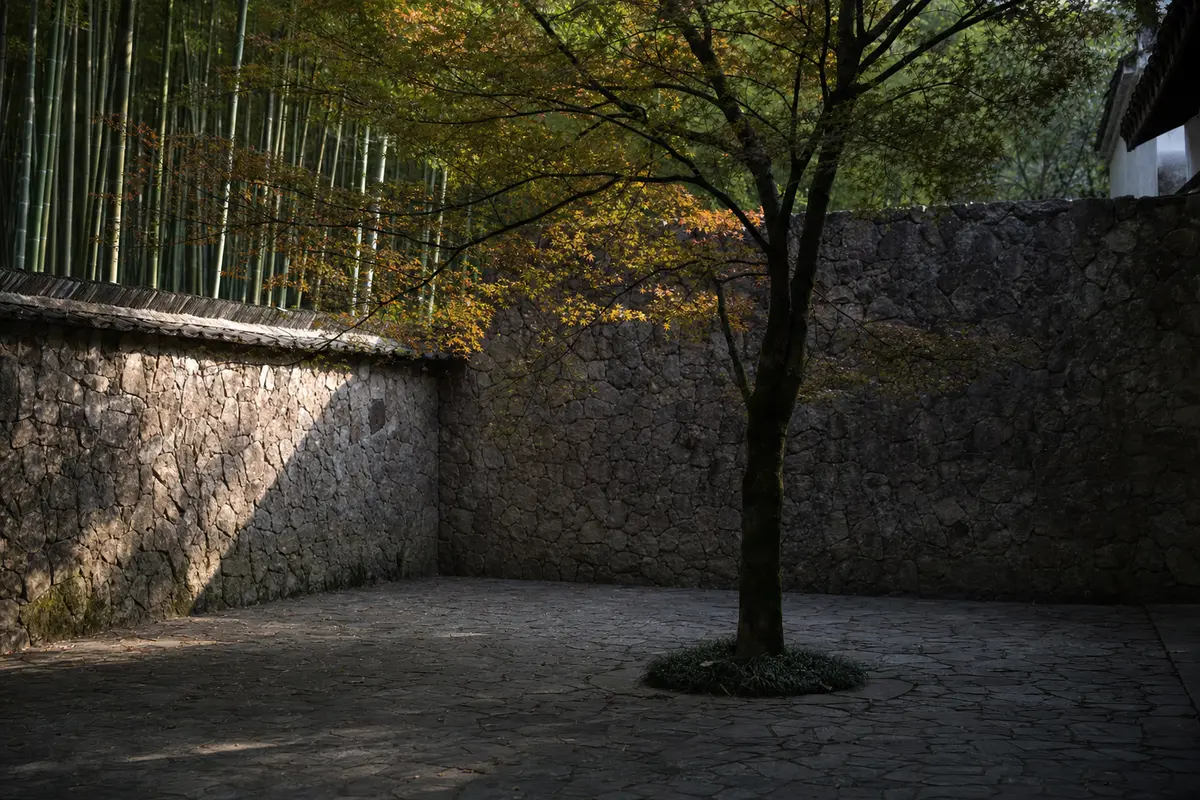 A quiet stone walled hotel courtyard with a single mature tree at its centre