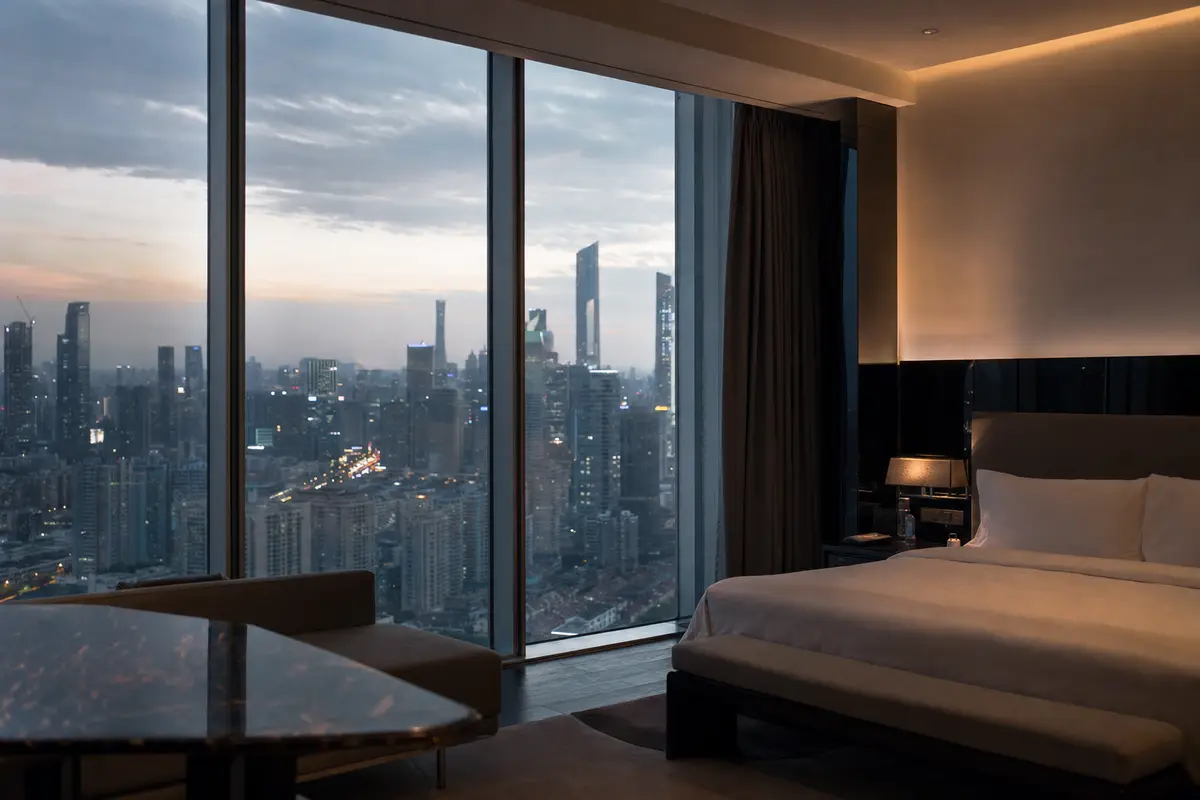 A city hotel room high above dense towers with floor to ceiling glass