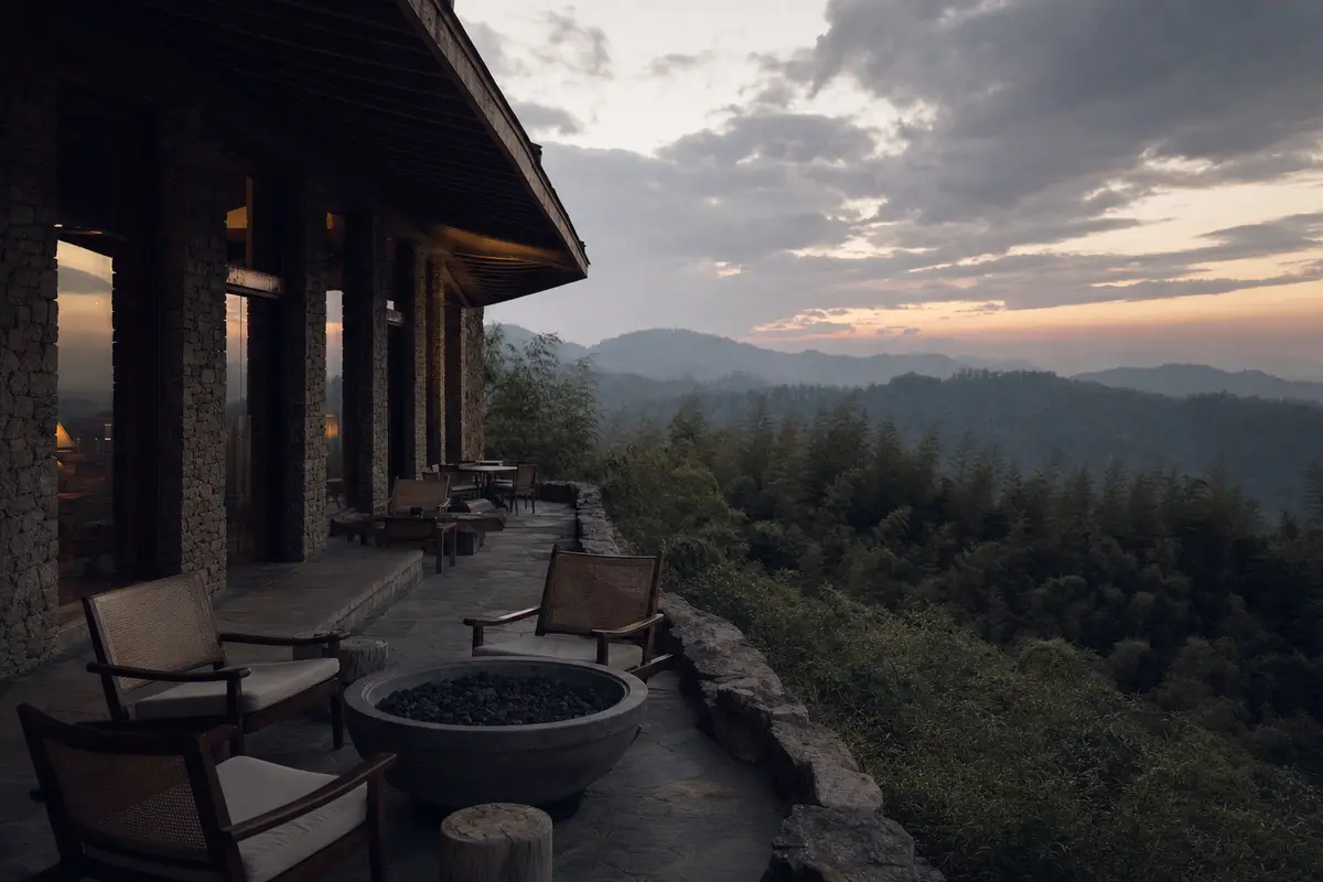 A stone and timber lodge terrace with deep eaves looking over bamboo ridges at dusk