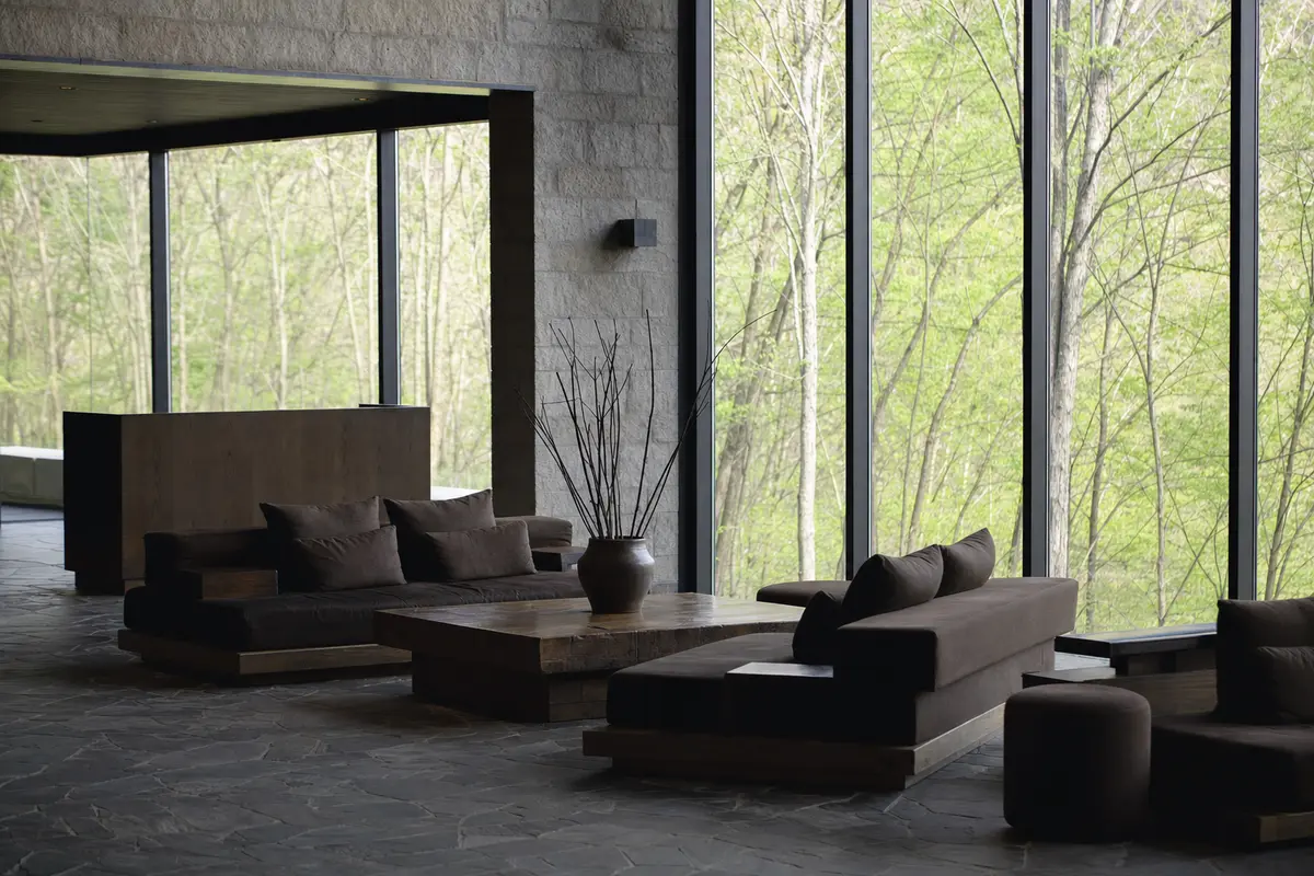 An empty resort reception lounge with low seating and tall windows onto forest