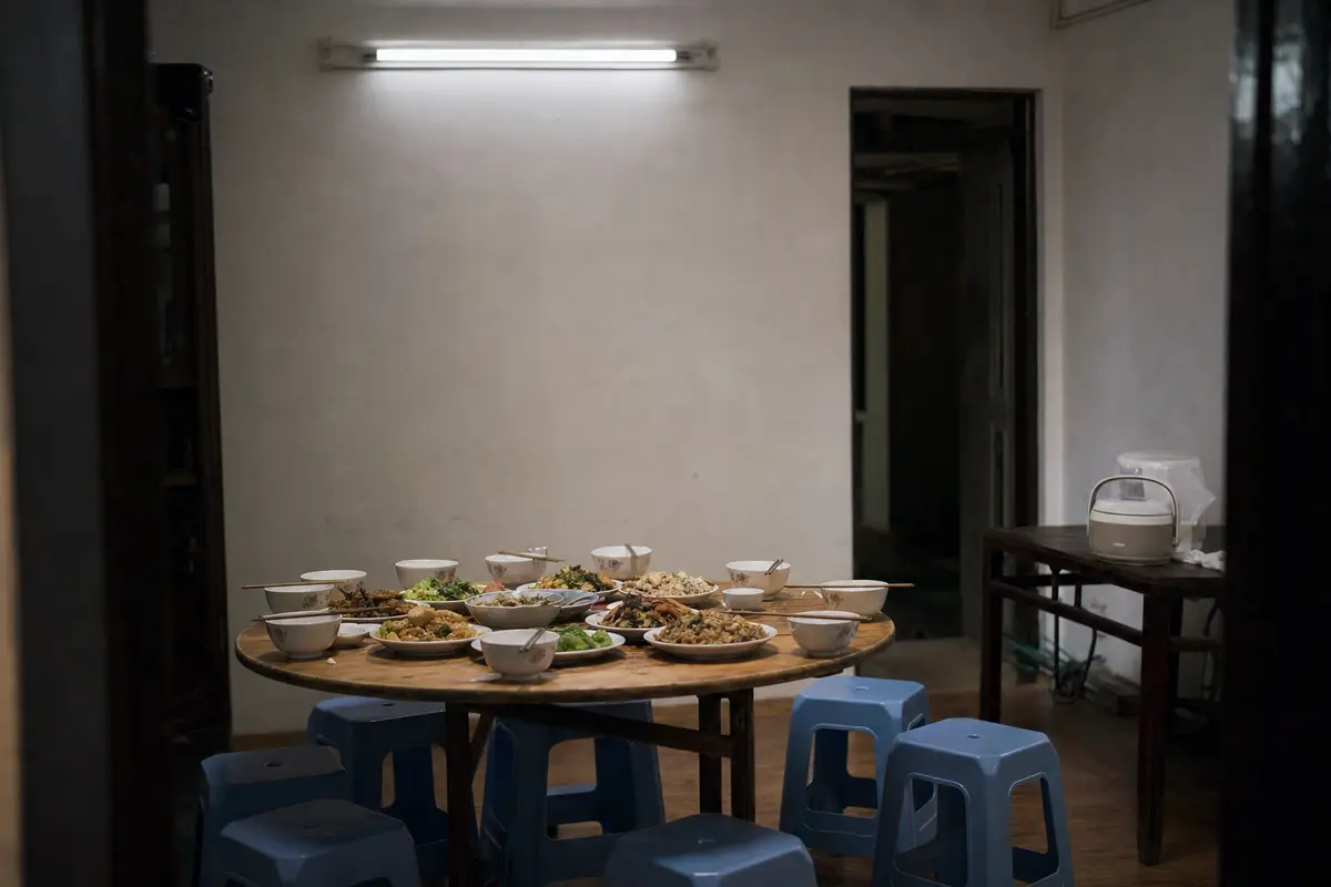 A round table laid with shared dishes in a guesthouse dining room with plastic stools
