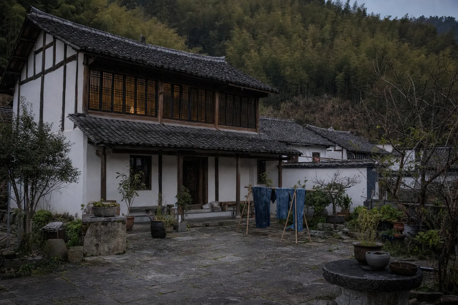 A lit upstairs window of a whitewashed village guesthouse above a stone courtyard at dusk