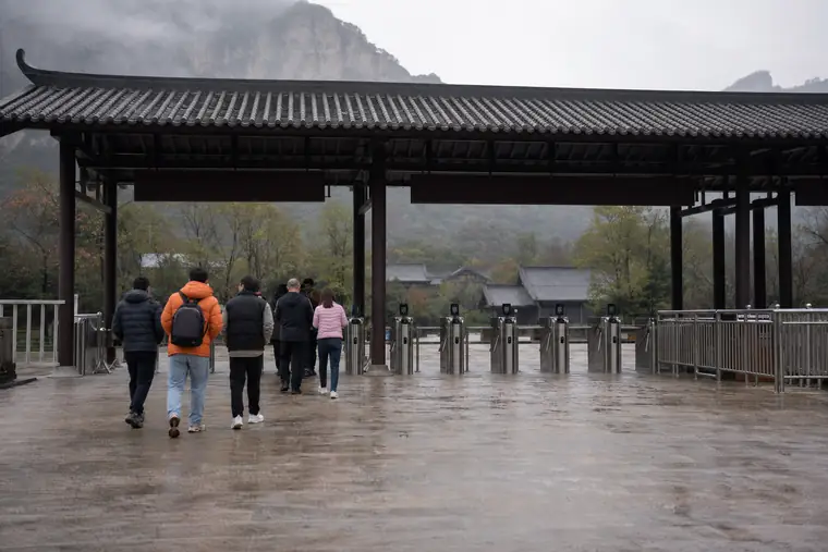 Visitors walking towards ticket gates under a tiled canopy in the rain