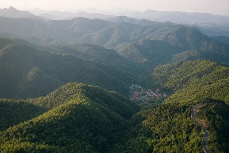 Layered forested ridges at first light with a village in the valley below